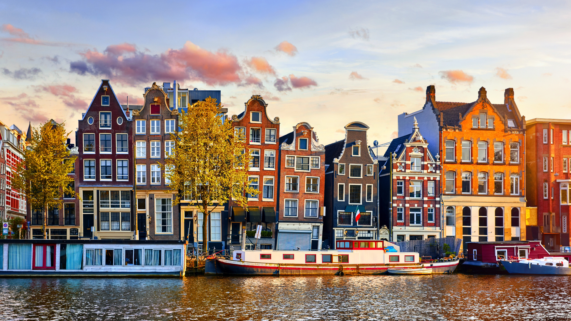 Colorful row of houses on a river with boats in Amsterdam